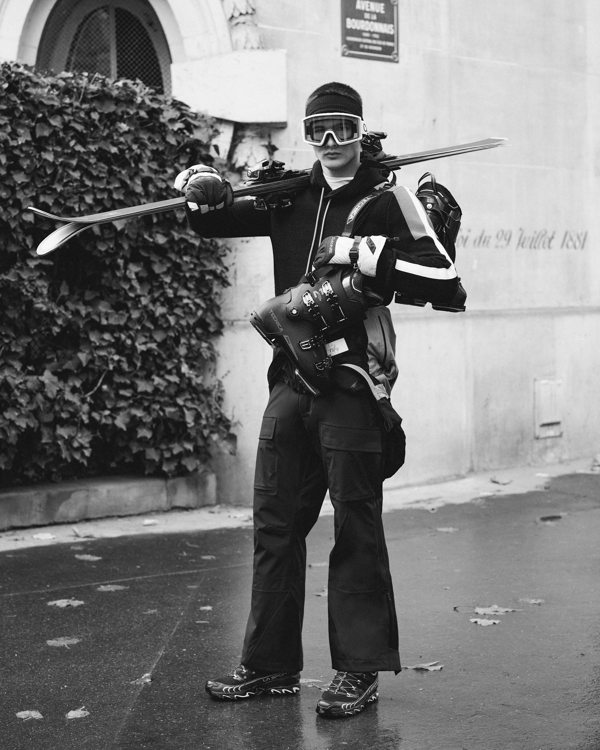 Person in winter gear with skis and goggles standing on a street.