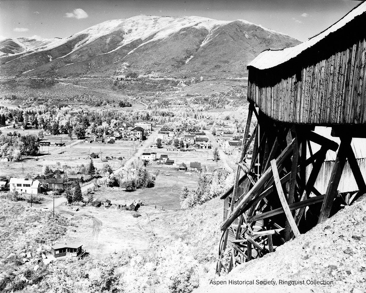 Vintage black and white photograph of a mountainous landscape with a wooden mining structure and town below.