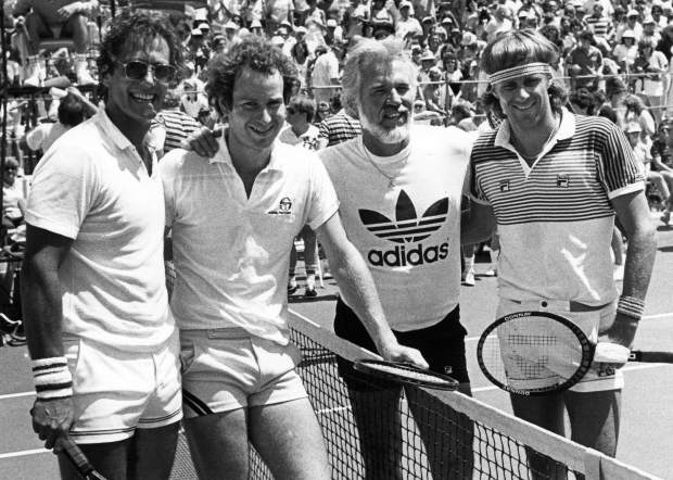 Vintage photo of four tennis players standing together on a court in front of a crowd.