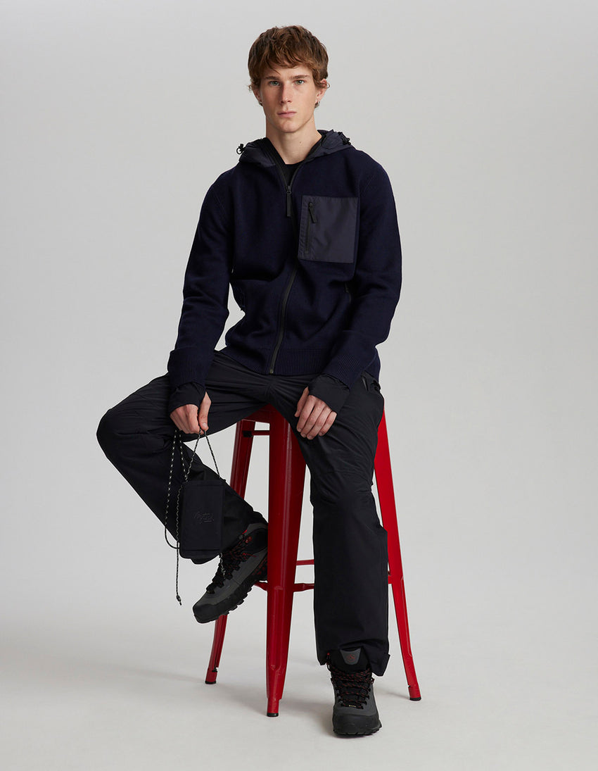 Man sitting on a red stool wearing a dark blue outfit against a plain background
