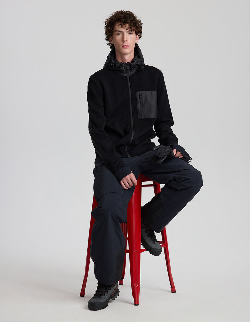 Person wearing a black outfit sitting on a red stool against a white background
