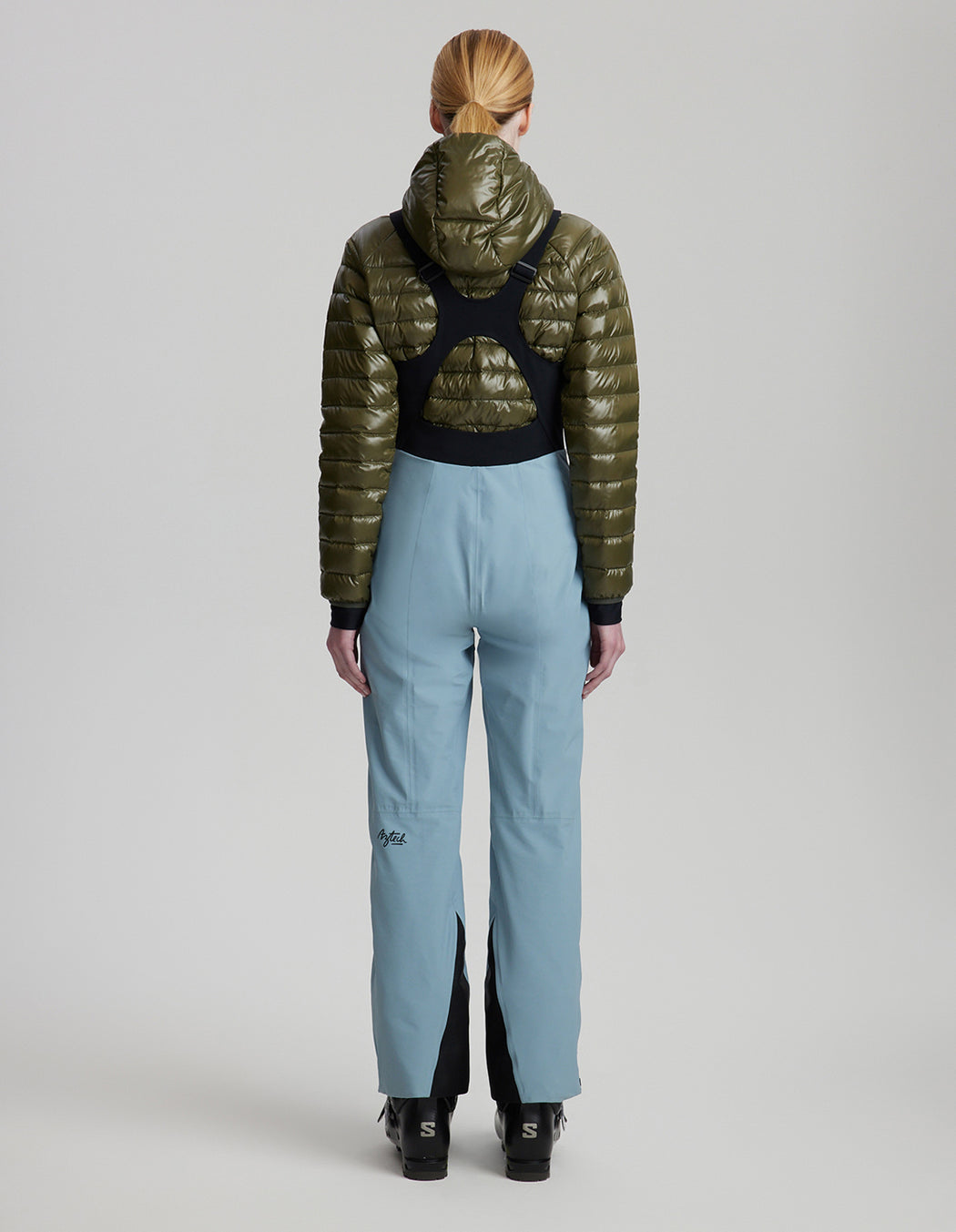 Person wearing a green puffer jacket and light blue pants on a gray background