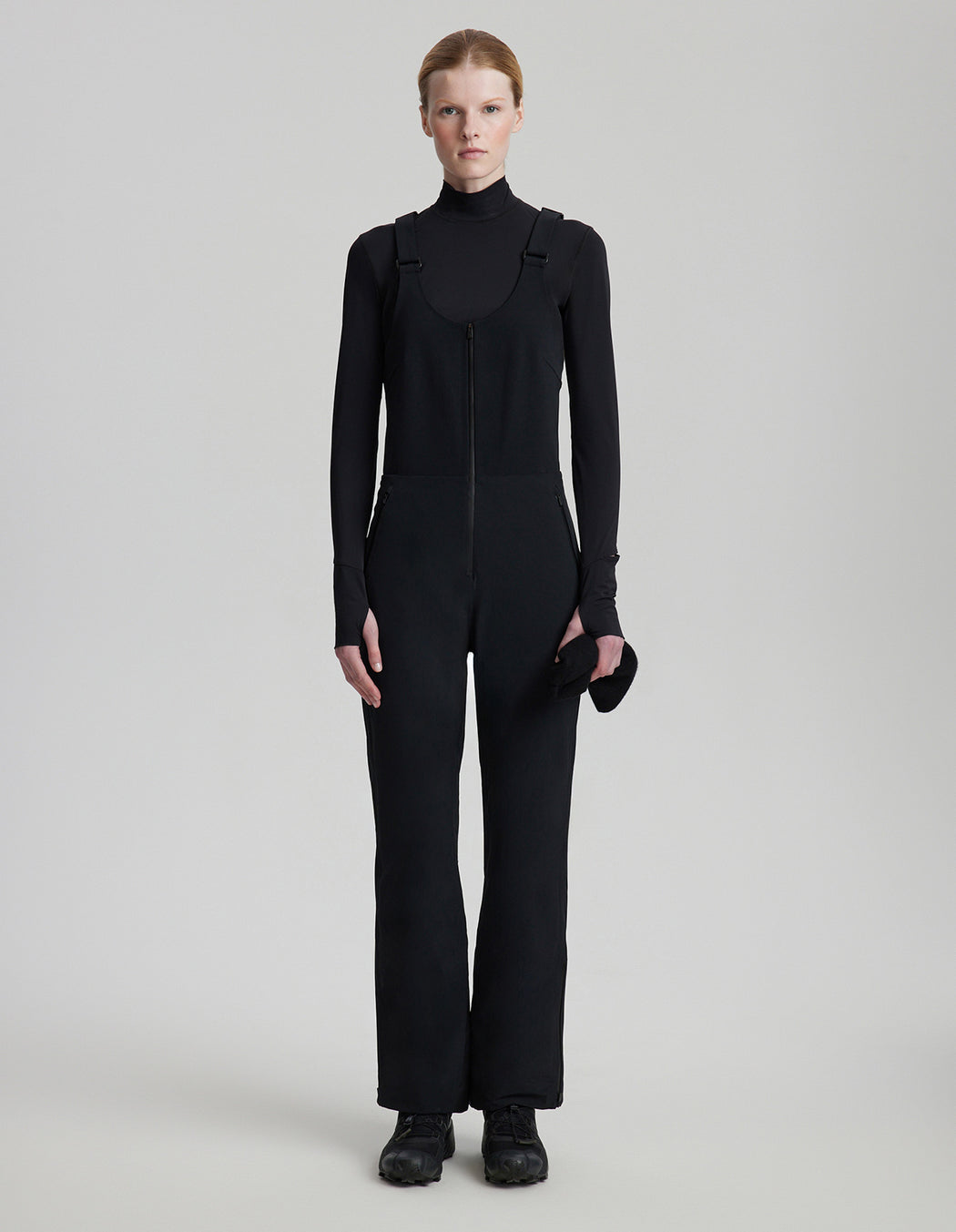 Person wearing a black jumpsuit on a light gray background