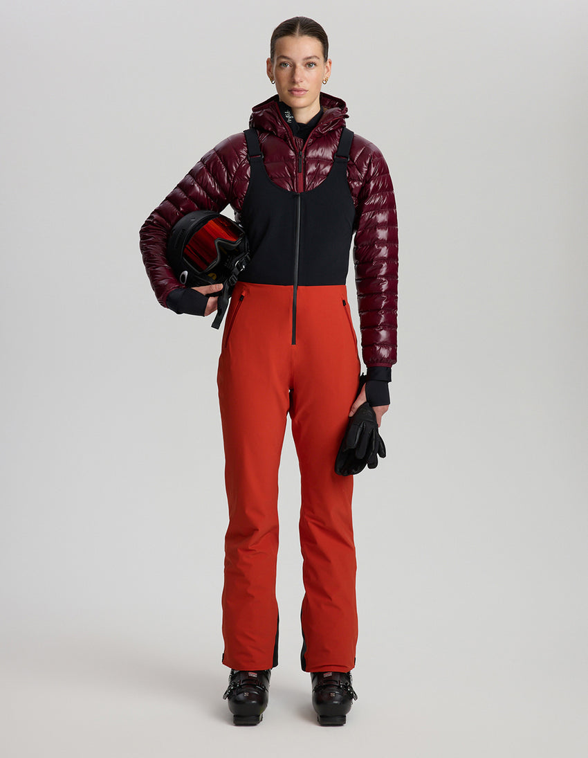 Person wearing a red and black ski outfit with a helmet on a light gray background