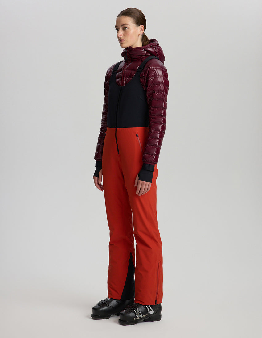 Person wearing a maroon and black jacket with red pants on a light gray background