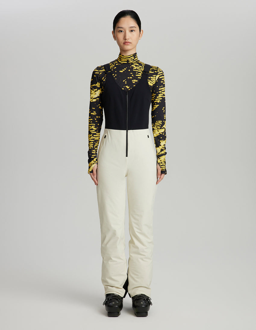 Person wearing a black and yellow patterned top with white pants on a gray background