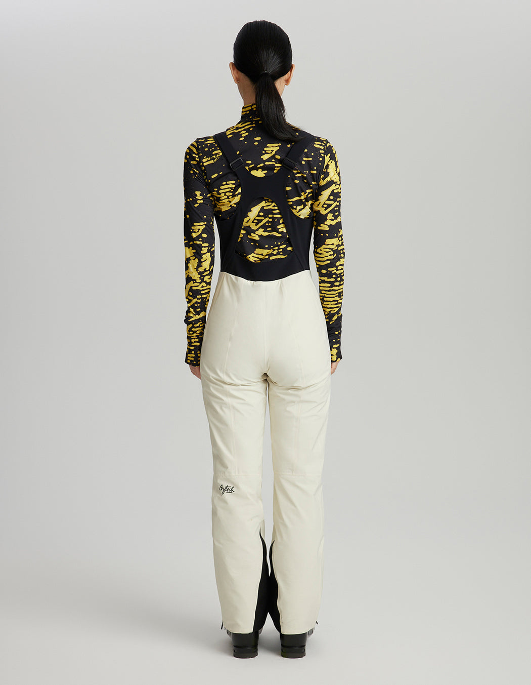 Person wearing a black and yellow patterned top with white pants on a gray background