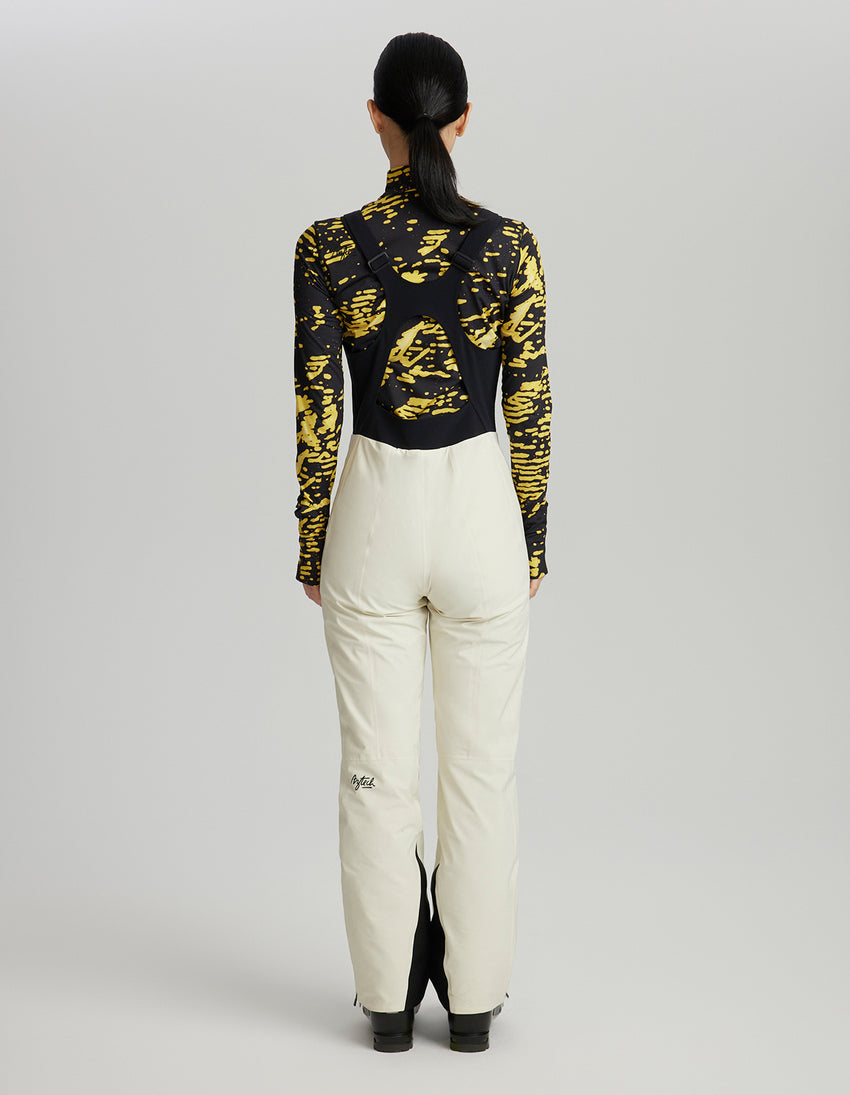 Person wearing a black and yellow patterned top with white pants on a gray background