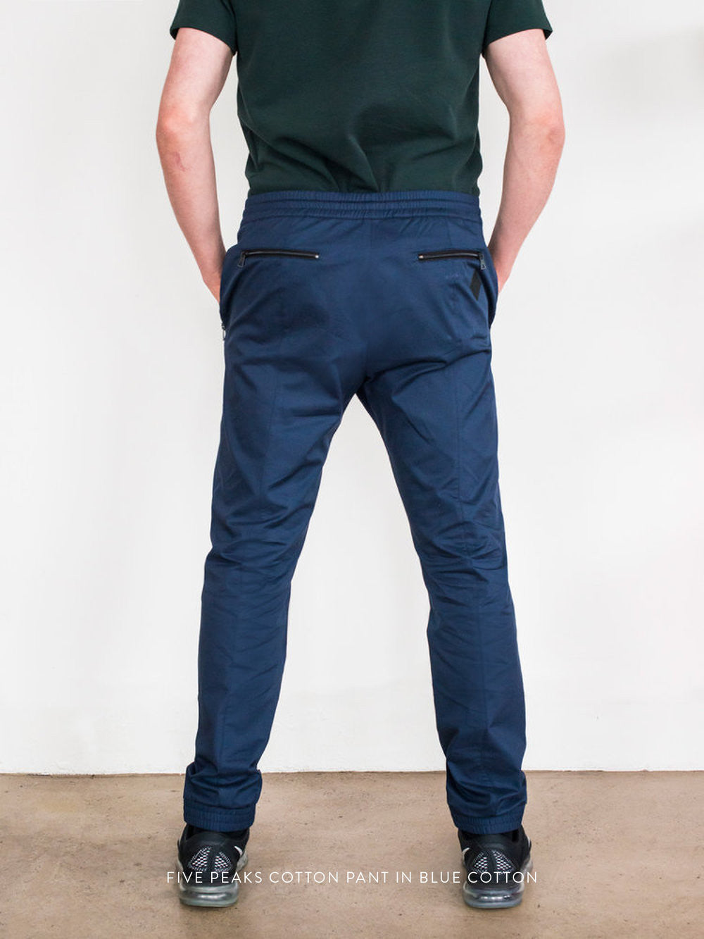Navy cotton pants with slim fit, back zip pockets, worn with black shoes and dark green shirt.