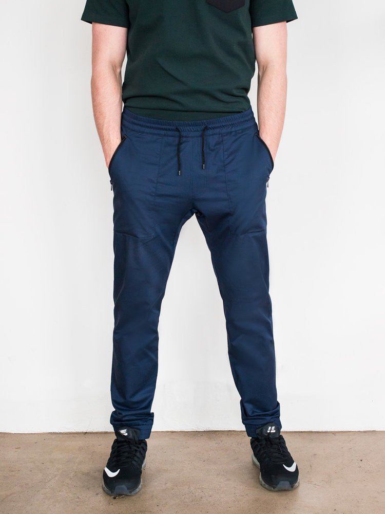 Navy cotton tapered pants with elastic cuffs and drawstring waist, worn with black sneakers.