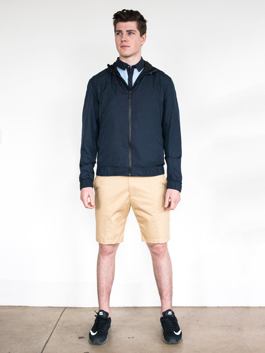 Men's khaki shorts paired with a navy zip-up jacket and black sneakers.